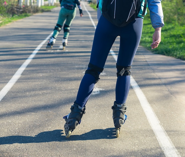 Twee meisjes op rolschaatsen rijden langs de weg Sportmeisjes Het ene meisje loopt het andere voor