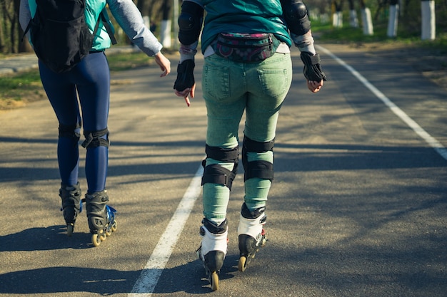 Twee meisjes op rolschaatsen rijden naast elkaar over de weg. Sportieve meisjes. Uitzicht op benen.