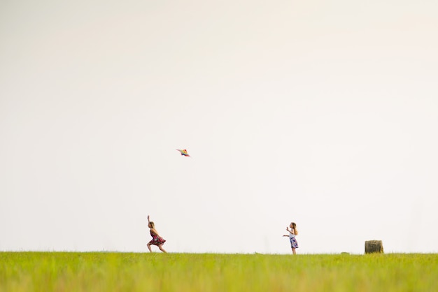 Twee meisjes rennen op een zomerveld met een vlieger