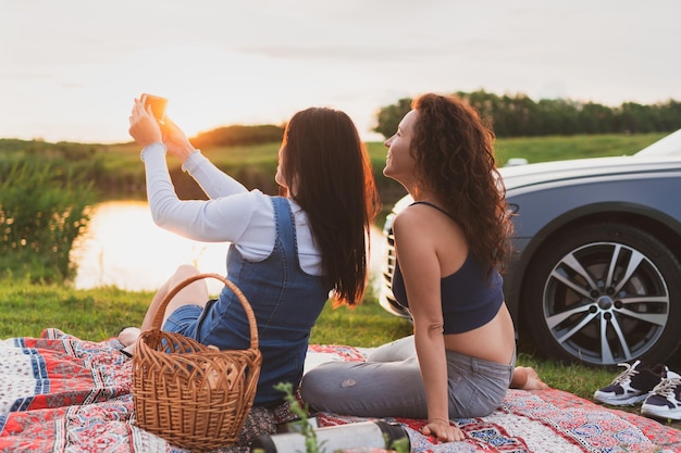 Twee meisjes rijden over de weg met een auto die langs de kant van de weg is gestopt en foto's maken met een smartphone vakantieconcept