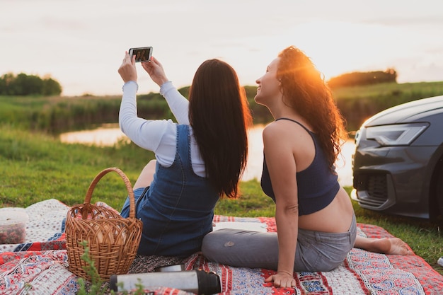 Twee meisjes rijden over de weg met een auto die langs de kant van de weg is gestopt en foto's maken met een smartphone Vakantieconcept