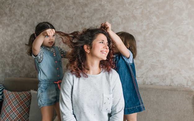 Twee meisjes spelen met hun moeder, doen haar haar, kammen haar haar. vrolijke en vrolijke moeder