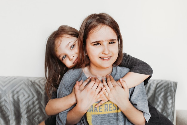 Twee meisjes, zussen spelen op de bank, knuffels, lachen, vechten, t-shirt