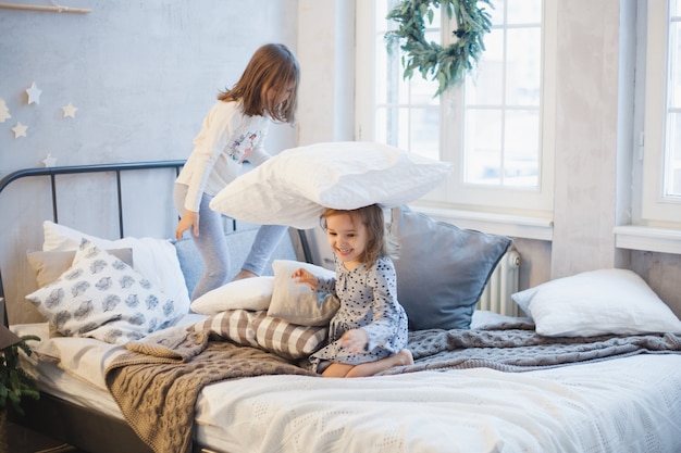 Twee meisjes, zussen vechten kussens op het bed, het raam versierd met een kerstkrans, leven, jeugd