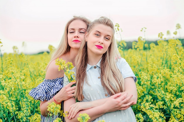 Twee meisjesmodellen die samen op camera op het koolzaadgebied stellen