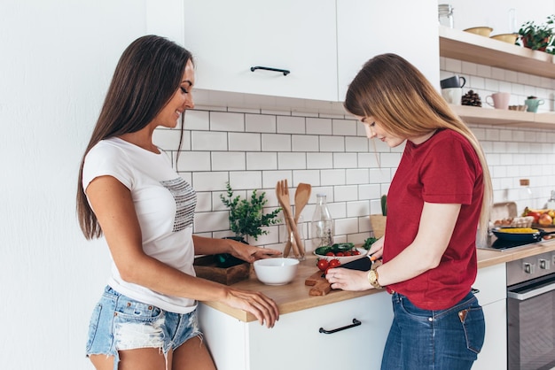 Twee meisjesvrienden die diner in keuken kokende salade voorbereiden