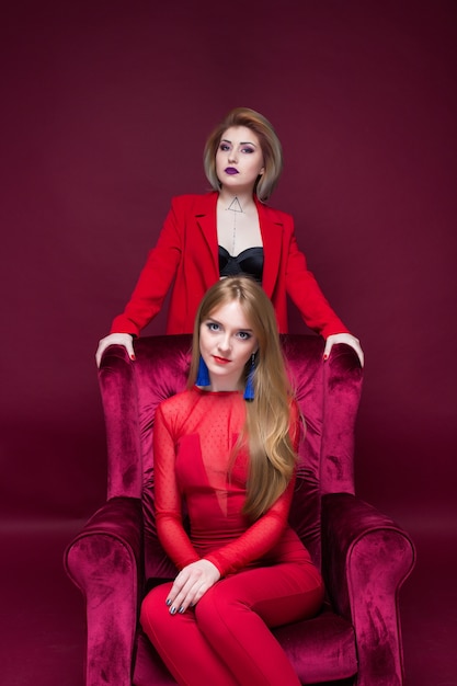 twee meisjesvrouw in rode kleren die rode stoel en rode achtergrond situeren