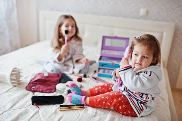 Twee meisjeszusters die make-up op het bed in de slaapkamer doen.