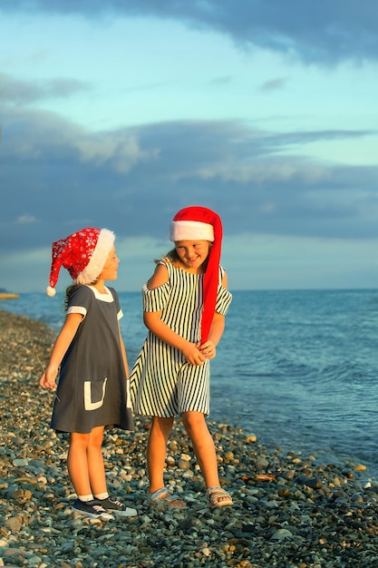 Twee meisjeszusters in kerstmanhoeden hebben plezier aan de kust bij zonsondergang