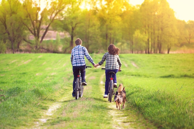 Twee mensen die fietsen, de een houdt een hond vast en de ander hand in hand houdt elkaars hand vast