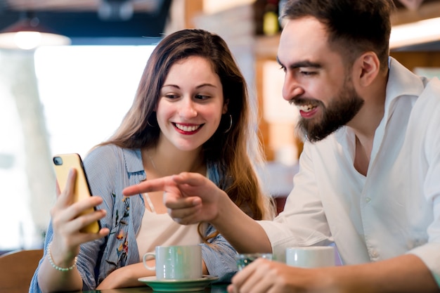 Twee mensen die samen een mobiele telefoon gebruiken terwijl ze een kopje koffie drinken in een coffeeshop.