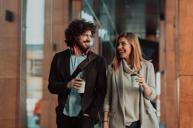 Foto twee mensen met een pauze van het werk lopen voor een modern bedrijf waar ze werken en koffie drinken.