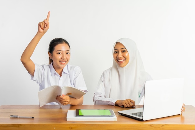 Twee middelbare schoolmeisjes zitten aan een bureau terwijl ze met hun vinger wijzen