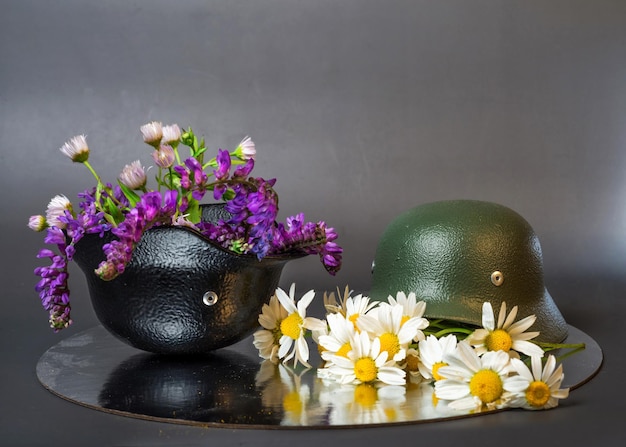 Twee mini-kopieën van militaire helmen met boeketten van wilde bloemen en madeliefjes