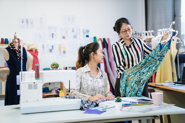 Twee modeontwerpers die naar een kledingstuk kijken en fouten controleren. jonge meisjescollega's die samen met nieuwe seizoensinzameling in workshop bespreken. groep vrouwelijke kleermakers die in studio werken