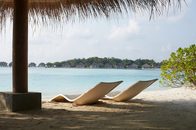 Twee moderne strandstoelen op het strand onder stroparaplu De kustlijn van de Indische Oceaan op het eiland Maldiven Witte zandstranden en kalme zee Reis- en vakantieconcept