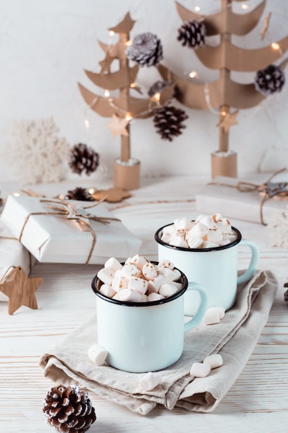 Twee mokken met cacao en marshmallows in kerstversiering op een witte houten tafel. Milieuvriendelijke vakantie. Verticale weergave