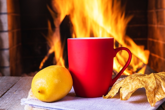 Twee mokken thee of koffie, herfstbladeren en citroen bij een gezellige open haard, in een landhuis, herfst- of wintervakantie, horizontaal.