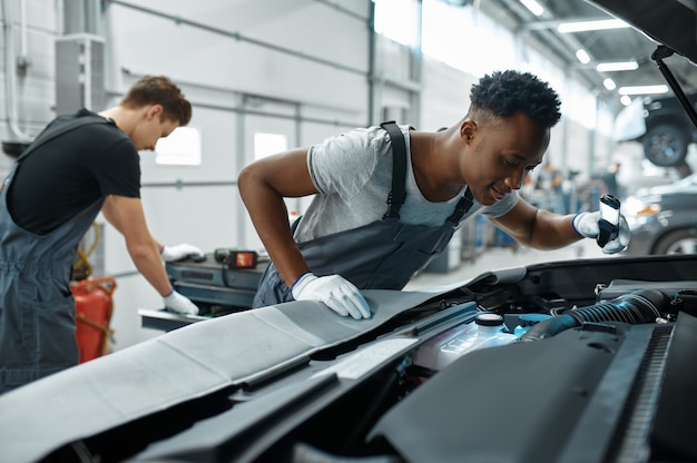 Twee monteur mannen inspecteert motor in mechanische werkplaats.