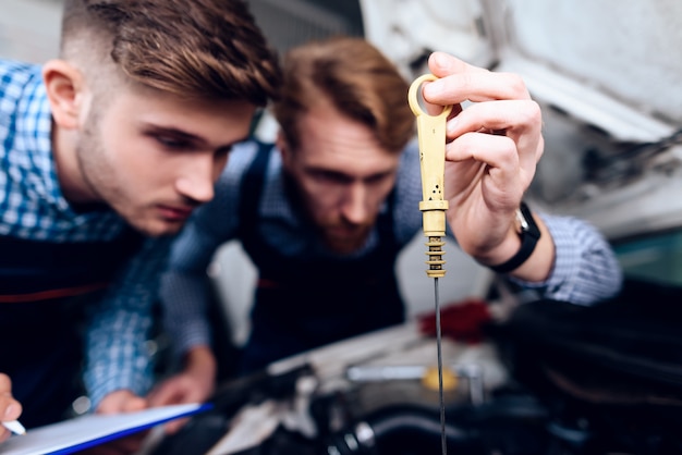 Twee monteurs controleren het oliepeil in de autoreparatiewerkplaats.