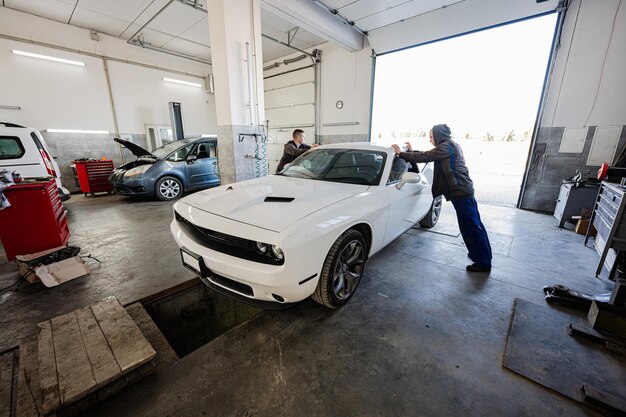 Twee monteurs van de serviceman in reparatiestation werken met een spierauto man-werknemer diagnosticeert het chassis