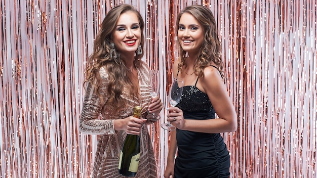 Twee mooie elegante vrouwen die champagne drinken tegen fonkelende decoratie