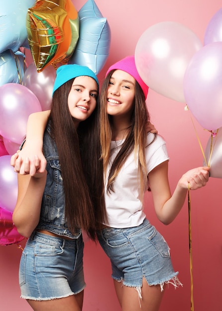 Twee mooie emotionele meisjes houden ballonnen vast en poseren tegen een roze muur