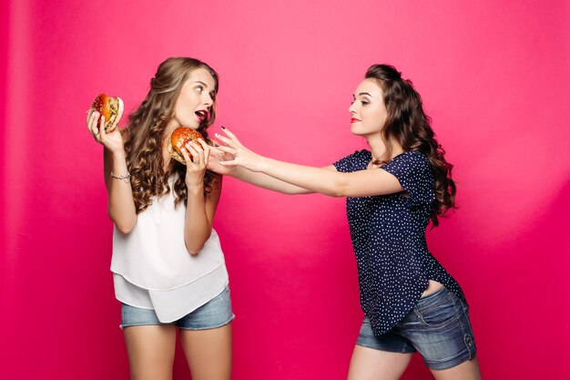 Twee mooie en hongerige meisjes die grote hamburger twee willen.