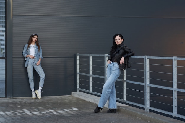 twee mooie en stijlvolle dames poseren bij een grijze muur in de straat