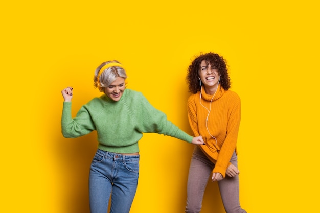 Twee mooie gekrulde haren vrouwen dansen terwijl u luistert naar muziek via een koptelefoon