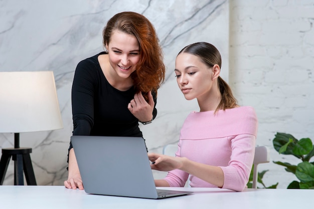 Twee mooie gelukkige vrouwenvrienden of collega's bekijken thuis de monitor van laptop computer