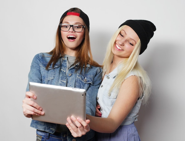 Twee mooie hipstermeisjes die een zelfportret met een tablet, over witte niet geïsoleerde achtergrond nemen