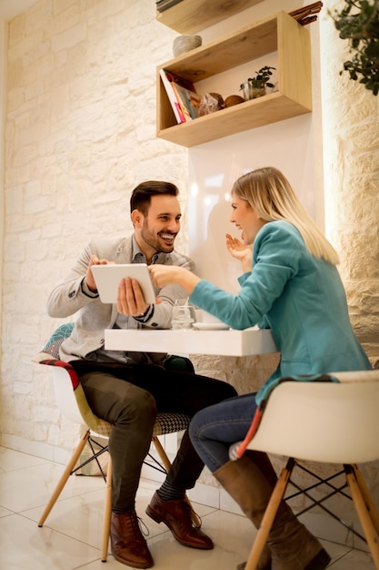 Twee mooie jonge lachende ondernemers zitten in café en werken aan digitale tablet.