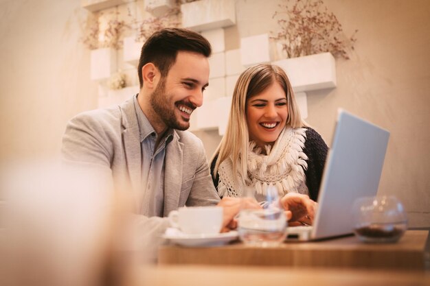 Twee mooie jonge lachende ondernemers zitten in café en werken op laptop.