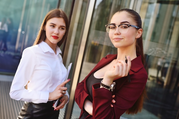 Twee mooie jonge vrouwen in zakelijke kleding op het oppervlak van een modern gebouw