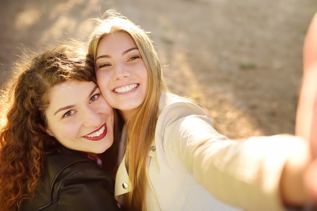 Foto twee mooie jonge vrouwen nemen selfie op zonnig park. vriendinnetjes.