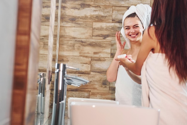 Twee mooie jonge vrouwen staan samen in de badkamer bij de spiegel en maken hun gezicht schoon.