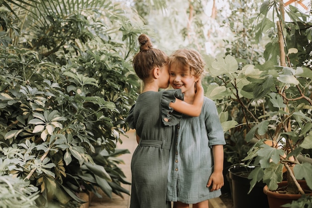 Twee mooie kleine meisjes lopen in de botanische tuin, omringd door tropische bladeren en bewaren geheimen