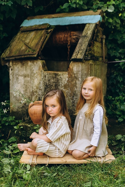 Twee mooie meisjes in witte antieke shirts in de buurt van een put op een achtergrond van gras en bomen