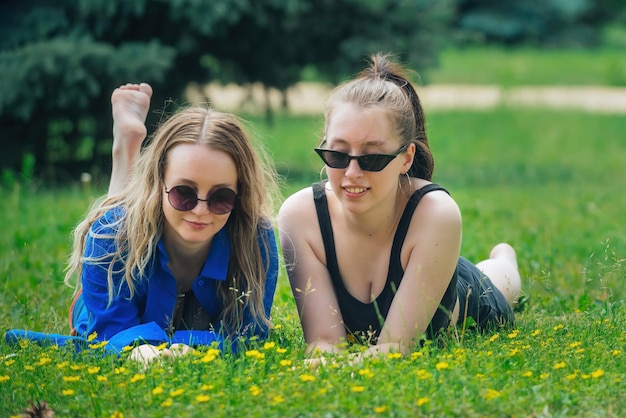 twee mooie meisjes liggen op het gras in het park en kletsen vrolijk