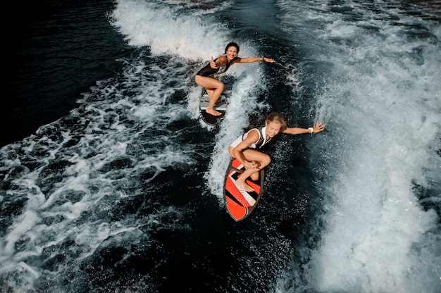 Twee mooie meisjes rijden op het wakeboard op het meer