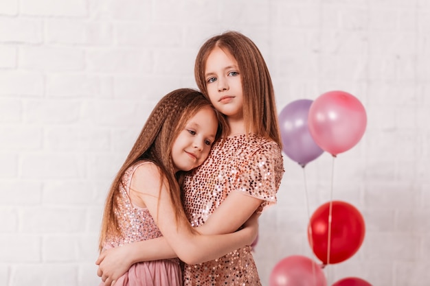 Twee mooie meisjes van schoolgaande leeftijd in blaffen in een witte kamer knuffelen