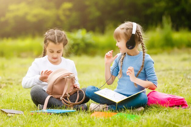 twee mooie schoolmeisjes zitten met boeken buiten in het park. Schoolmeisjes of studenten krijgen les in de natuur.