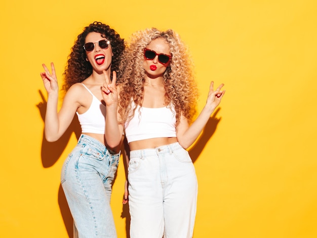 Twee mooie sexy lachende hipster vrouwen in rode zomer badmode badpakken Trendy modellen met afro krullen kapsel plezier in studio hete vrouw geïsoleerd op geel in zonnebril