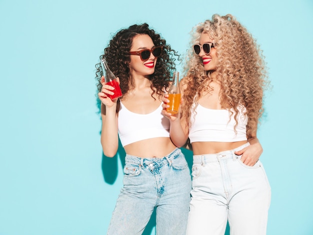 Twee mooie sexy lachende hipster vrouwen in zomerkleren Trendy modellen met afro krullen kapsel plezier in studio hete vrouw geïsoleerd op blauw gelukkig en vrolijk