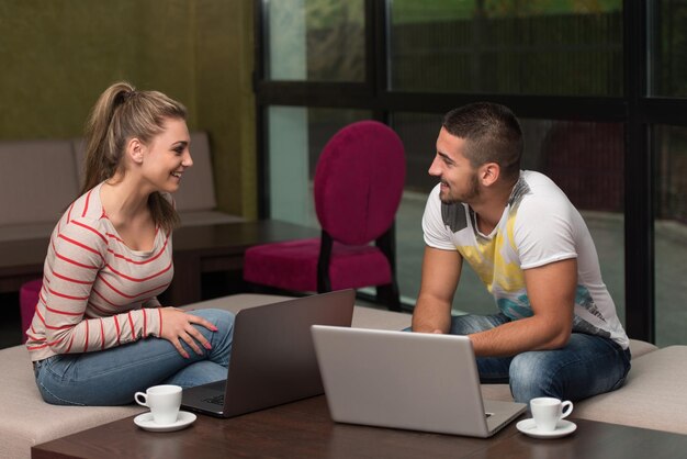 Twee mooie studenten drinken en hebben plezier met laptop in cafetaria