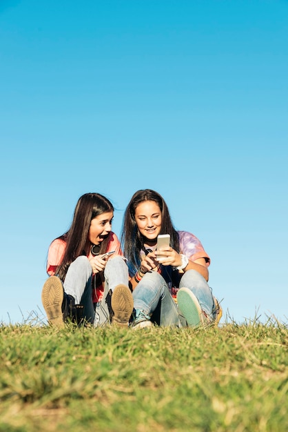 Twee mooie tienermeisjes die mobiel in het park gebruiken