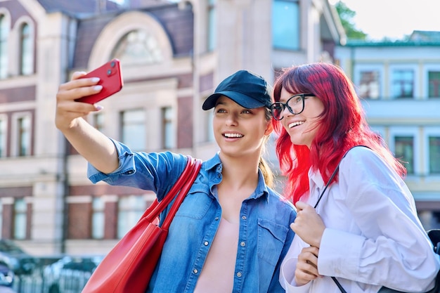 Twee mooie tienervrouwen die plezier hebben met het maken van selfie-portret op een smartphone buiten in de stad Adolescentie emoties geluk vriendschap vrijetijdsvakanties vreugde jeugdconcept