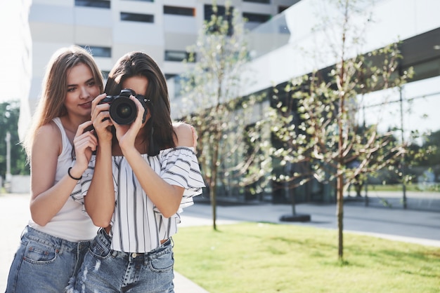 Twee mooie vriendinnen van het meisje met de camera maken samen foto's en wandelen door de stad