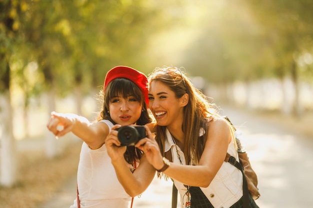 Twee mooie vrolijke vriendinnen maken foto's terwijl ze langs de zonnige laan lopen.